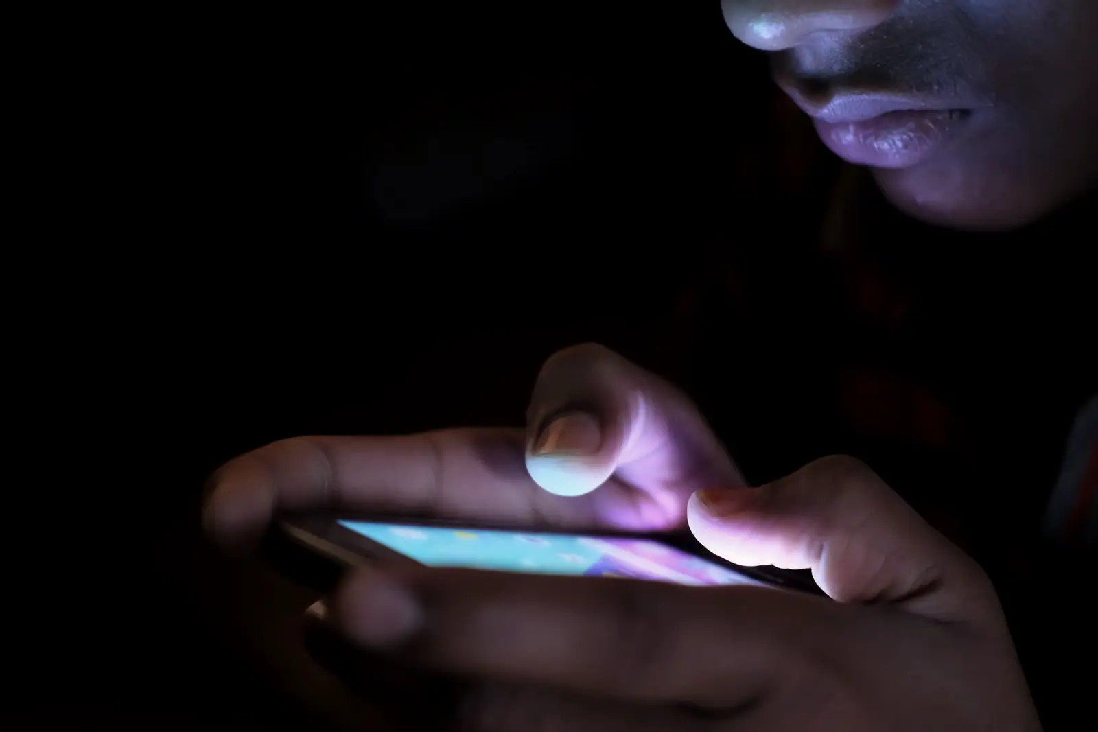 Des mains tiennent un téléphone allumé dans le noir